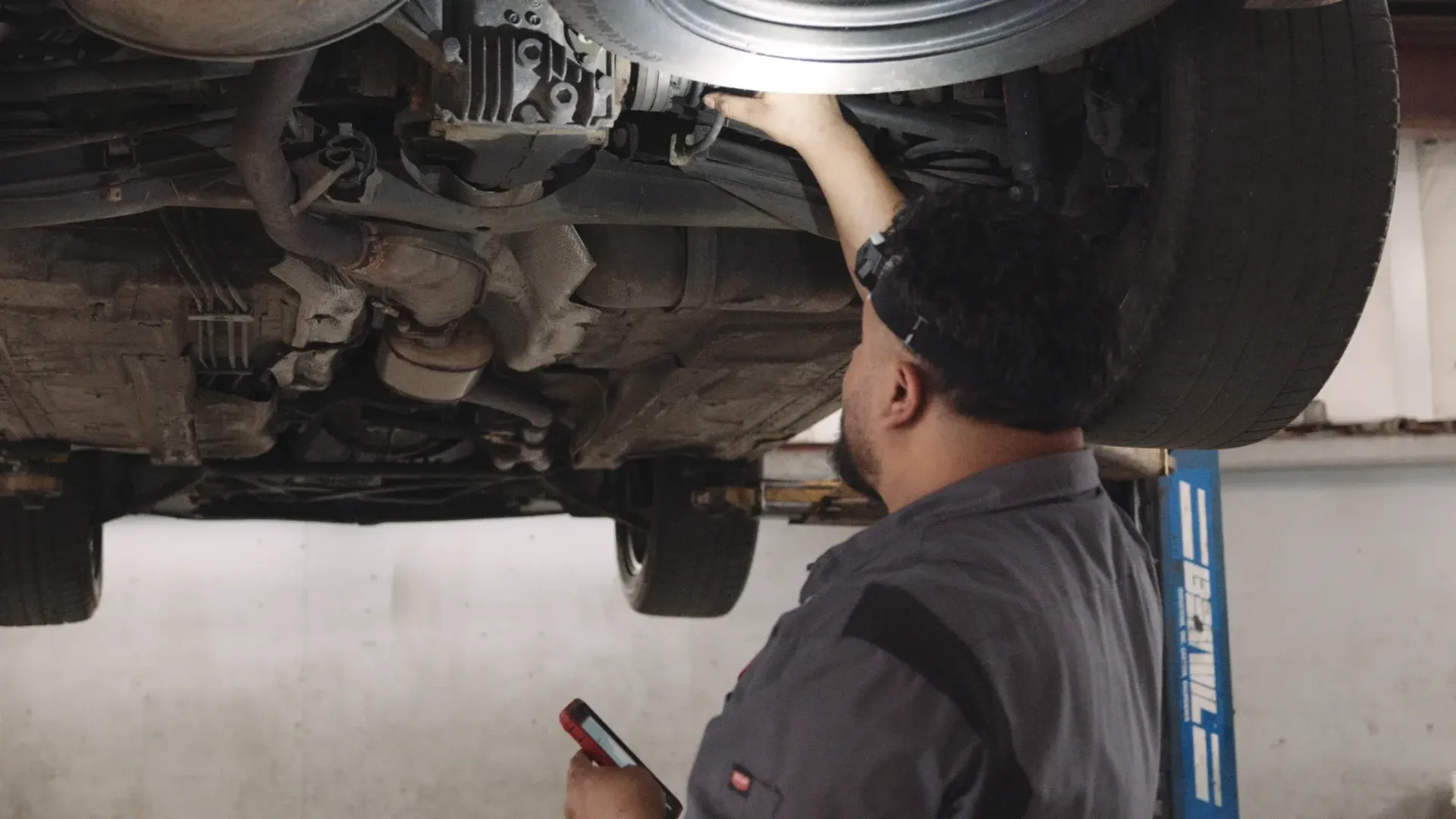Mechanic inspecting underside of a vehicle raised on a lift, holding a flashlight.