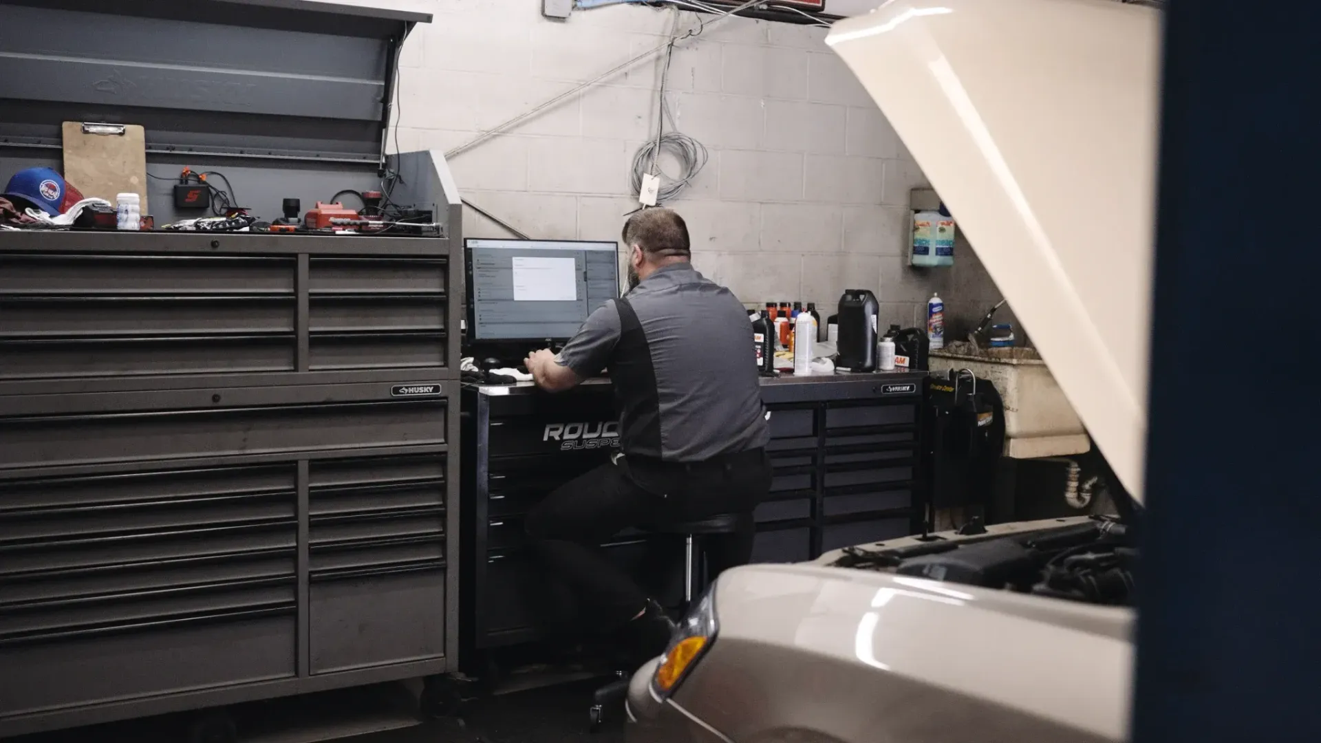 Mechanic using a computer in a garage with a car's hood open.