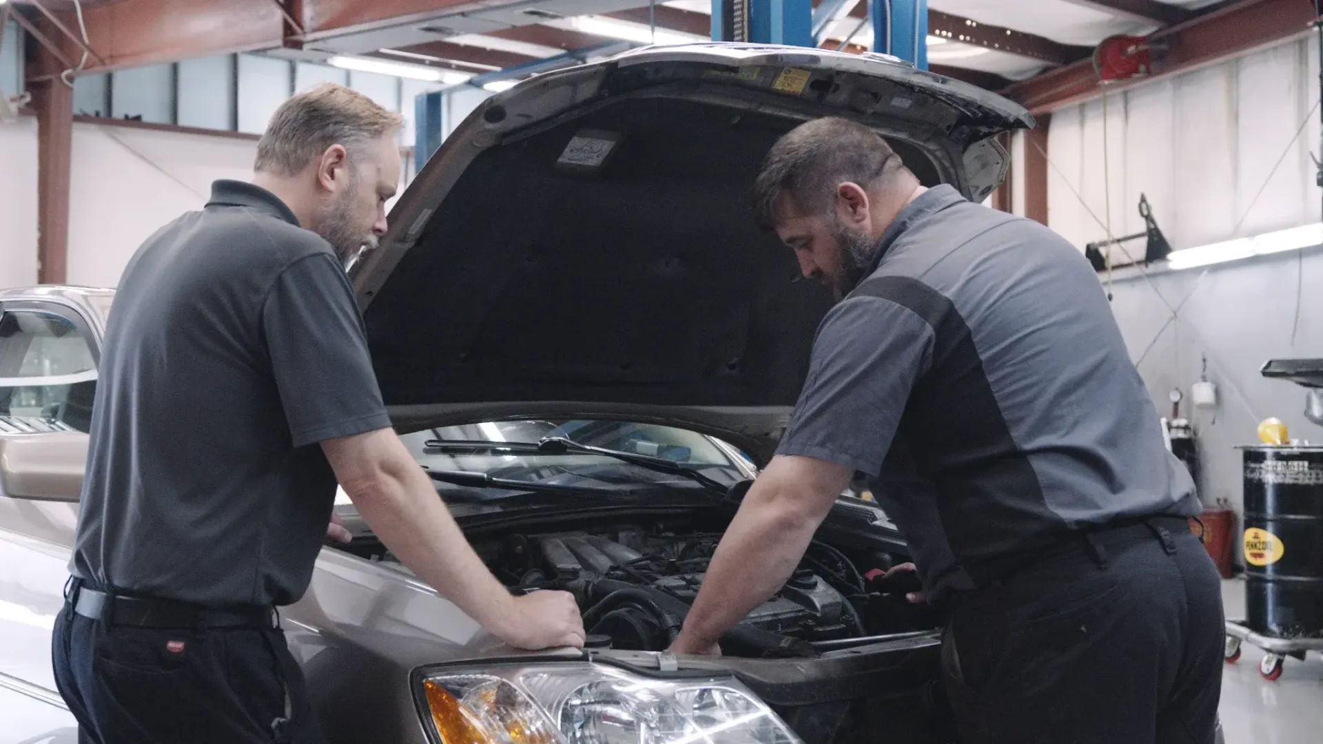 Two mechanics examining a car engine with the hood open in a garage.