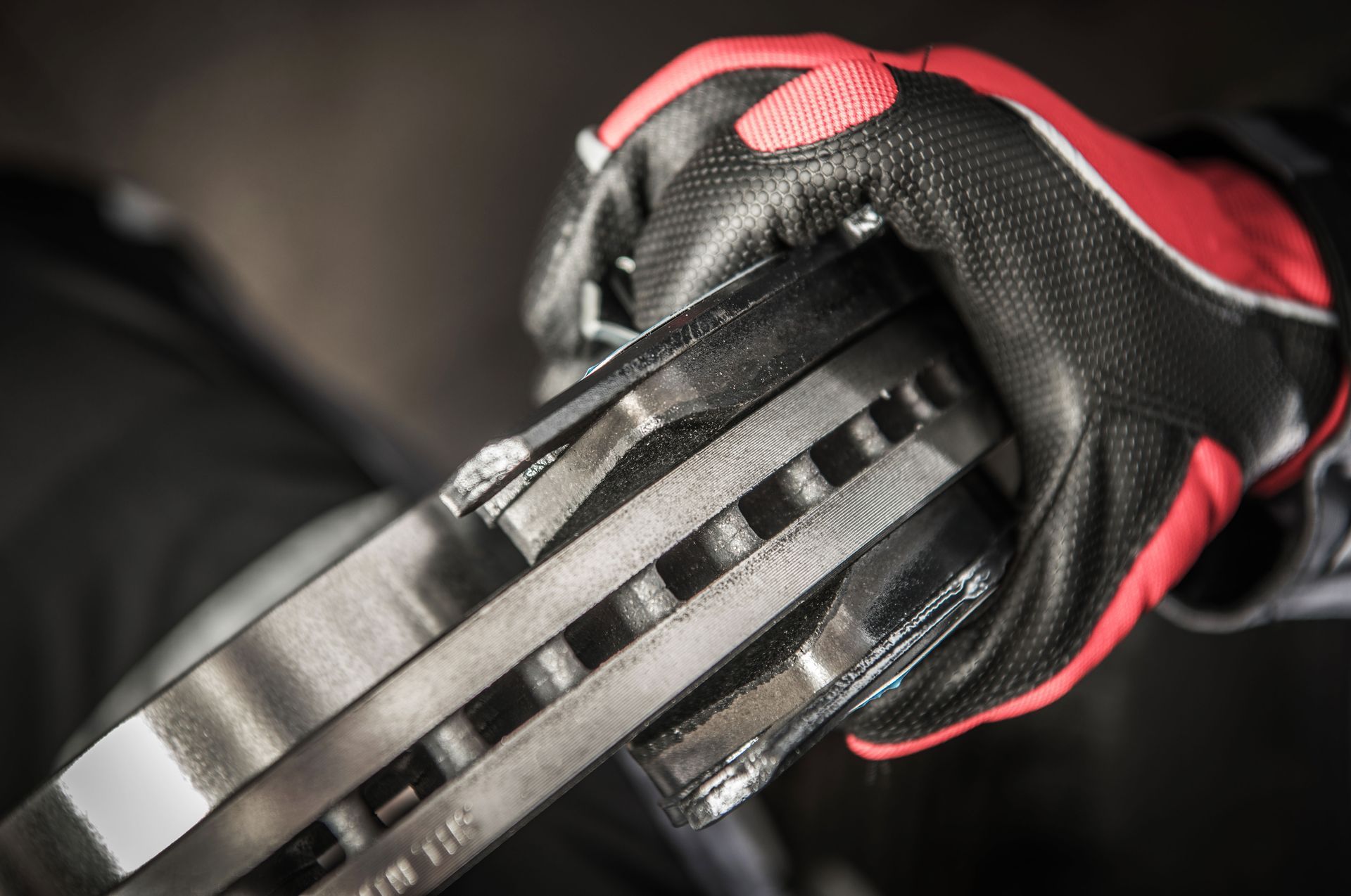 Gloved hand holding brake rotors; red, black, and white accents on glove.