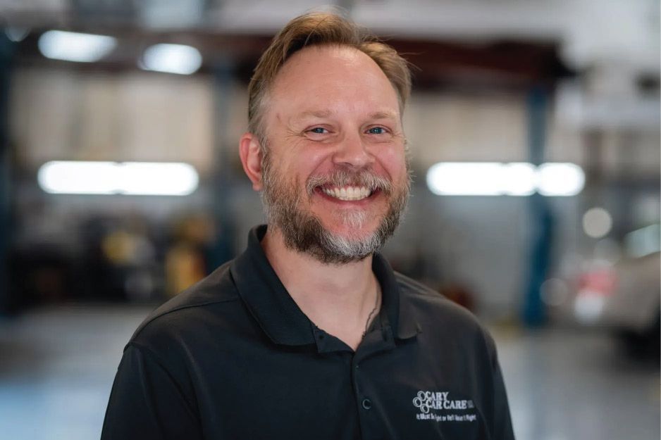 Man with a beard smiles, wearing a black shirt with a logo, in a garage.