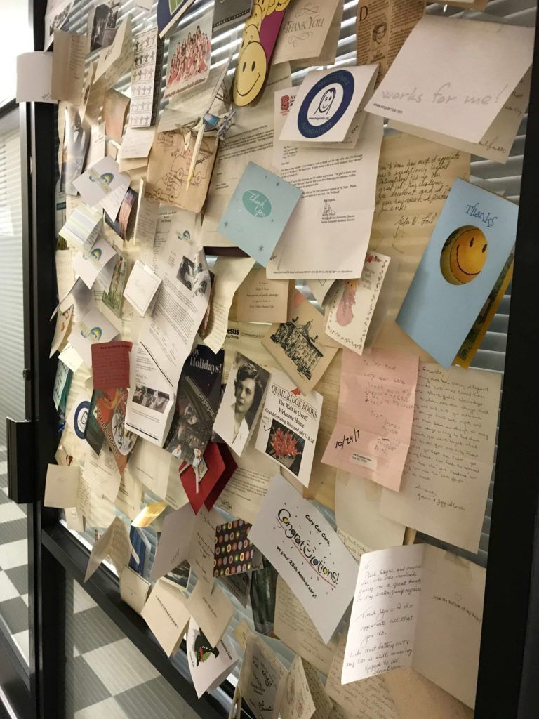 Assorted papers, cards, and notes pinned to a glass door. Varying sizes, colors, and handwriting are visible.