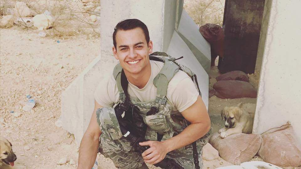 A man in a military uniform is kneeling down with a dog.