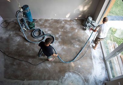 Two men are working on a concrete floor with a vacuum cleaner.