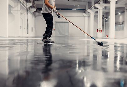 A man is painting a concrete floor with a broom.