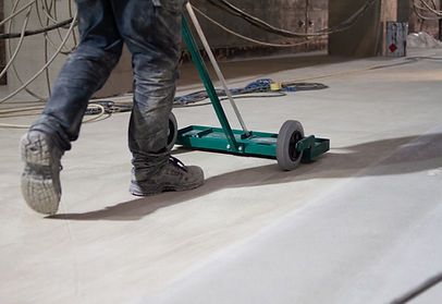 A man is walking on a concrete floor with a broom.
