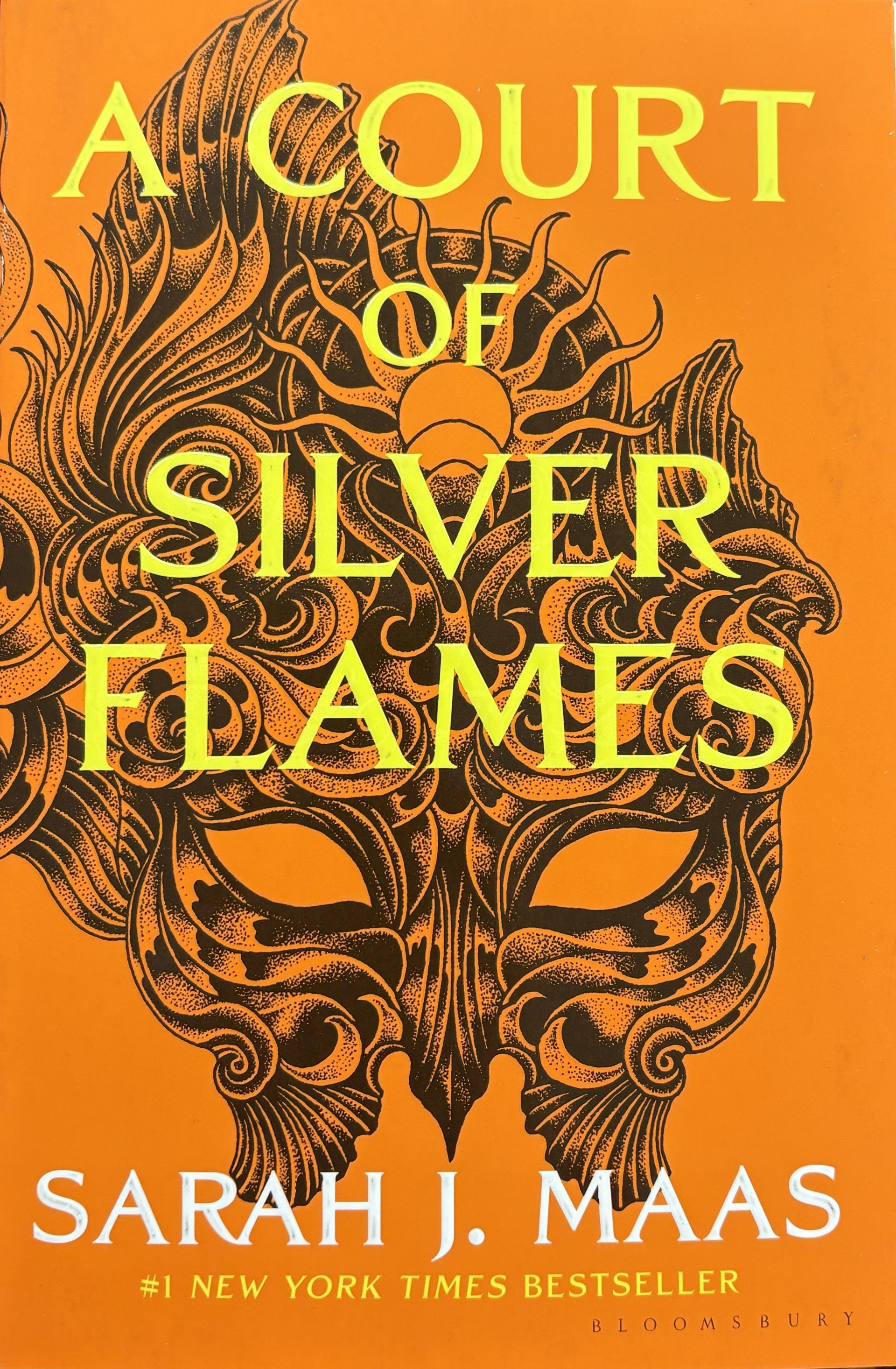 Book cover with mask on orange background titled "A Court of Silver Flames" by Sarah J. Mass