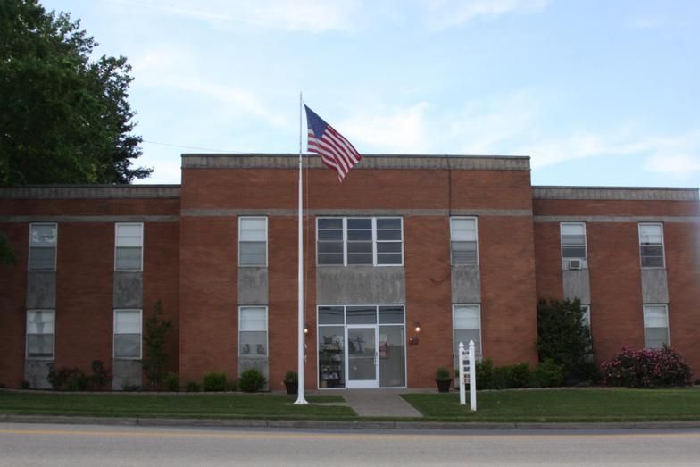 Brick building with an American flag flying on a pole in front. White doors and windows visible.