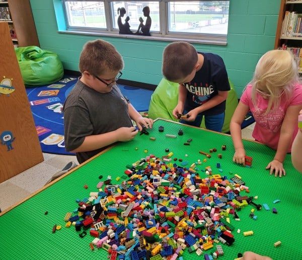 Children building with colorful LEGO bricks on a green table in a library.