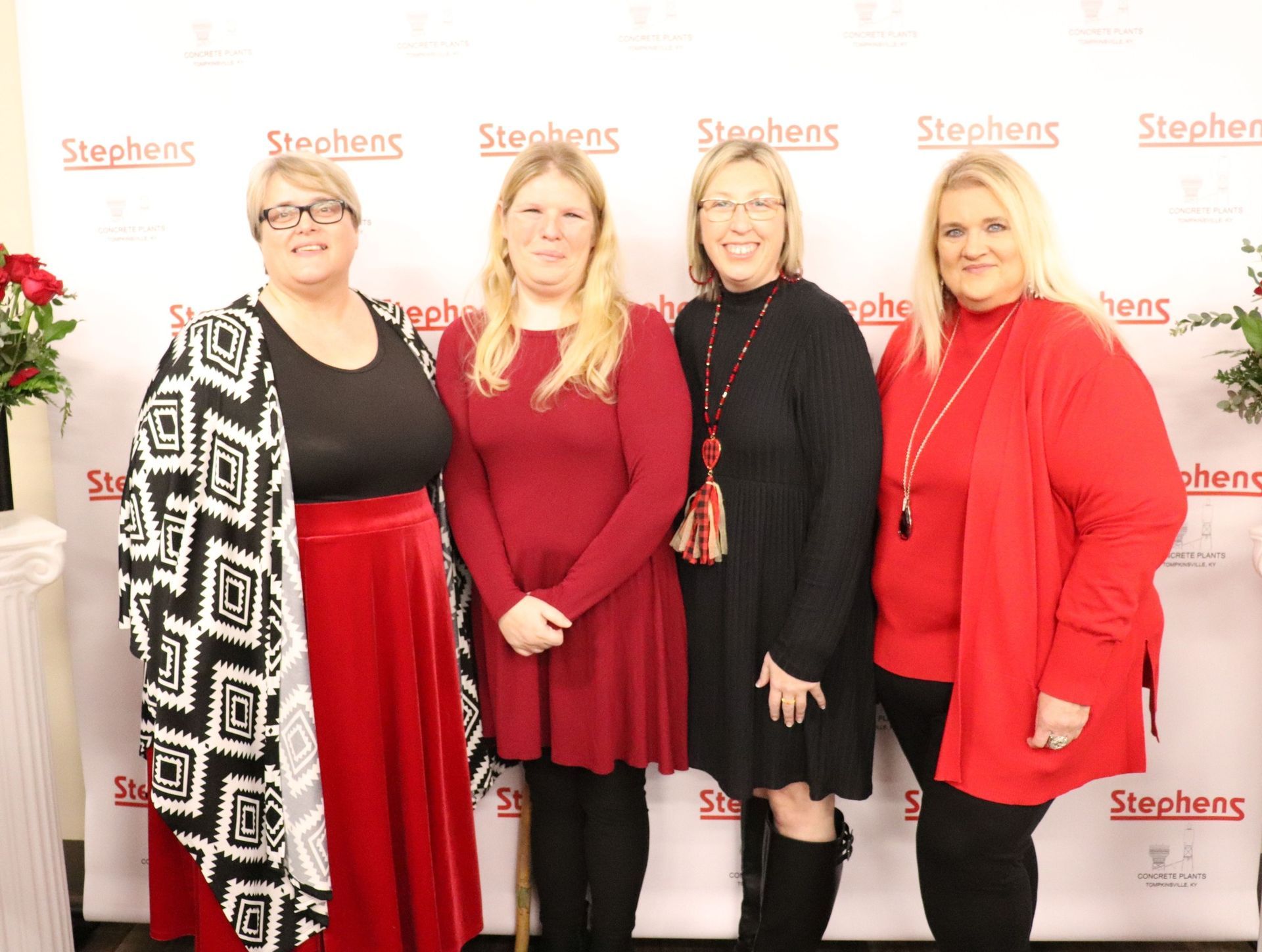 Four women posing for a photo. Three are wearing red. One woman in a black and white patterned jacket. 