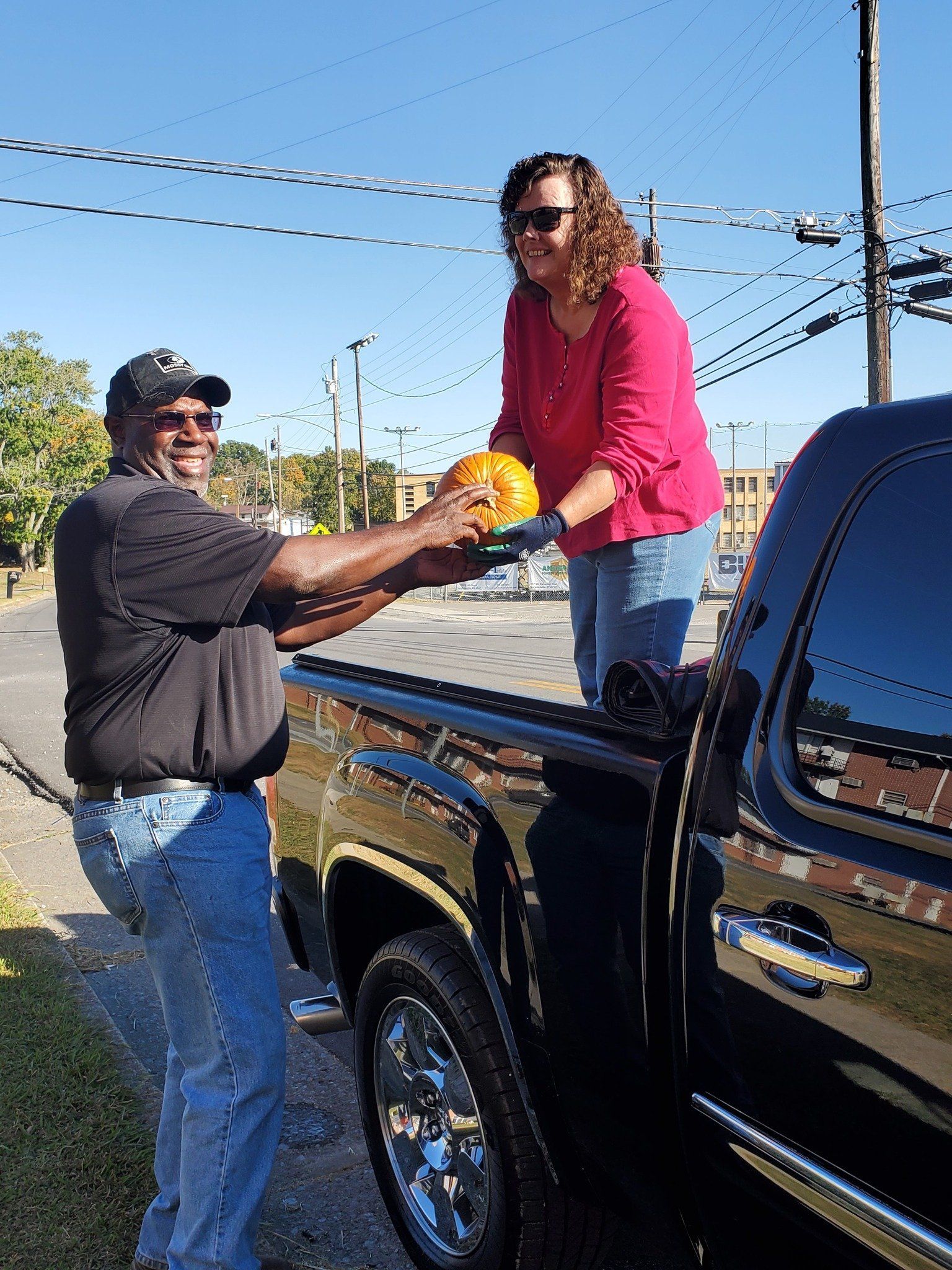 Man handing pumpkin to woman from a truck bed on a sunny day.