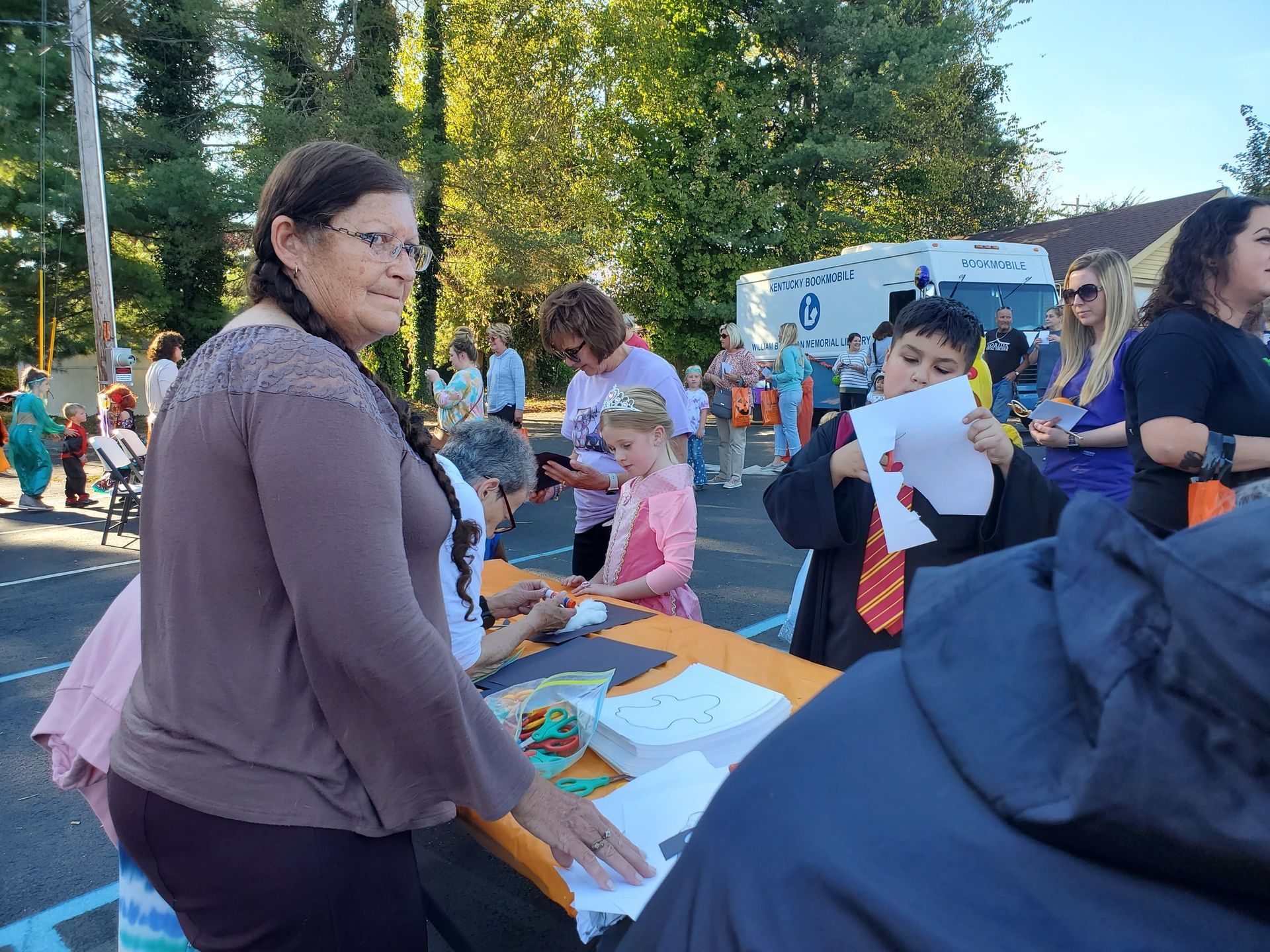 People at an outdoor event with a table; a child in costume holds up a drawing.
