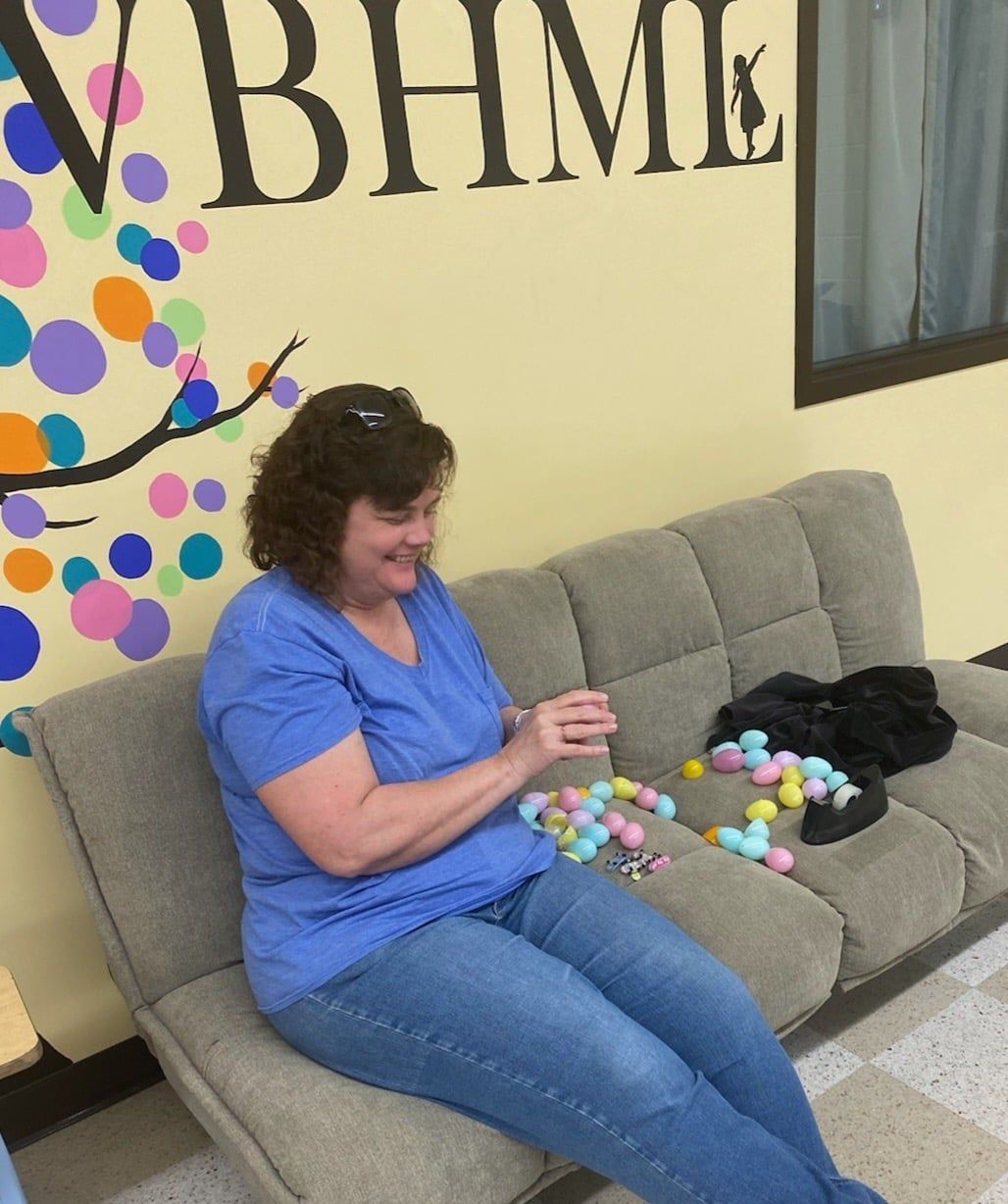 Woman sitting on a couch, smiling, sorting Easter eggs. Colorful wall decor and eggs on the couch.