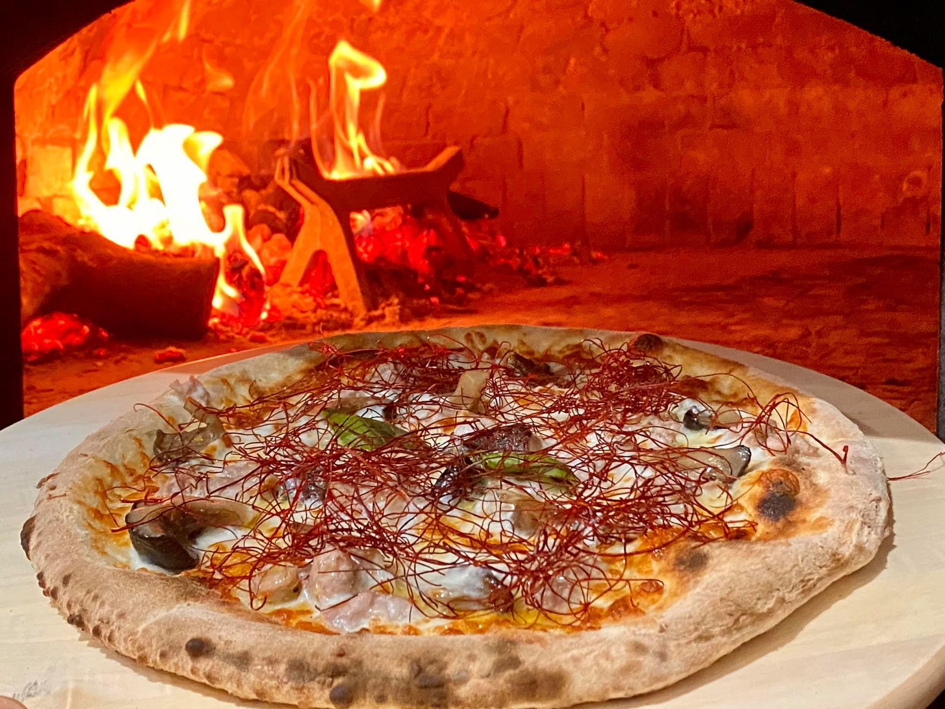 Pizza davanti al forno a legna; fiamme sullo sfondo.