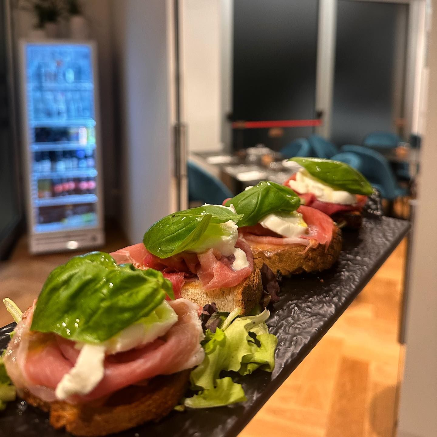 Bruschetta con prosciutto, mozzarella e basilico su un piatto scuro. Ambiente da ristorante.
