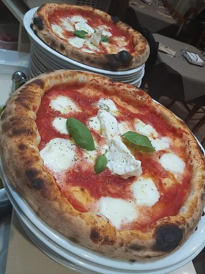 Due pizze con salsa rossa, mozzarella e basilico su piatti bianchi impilati.