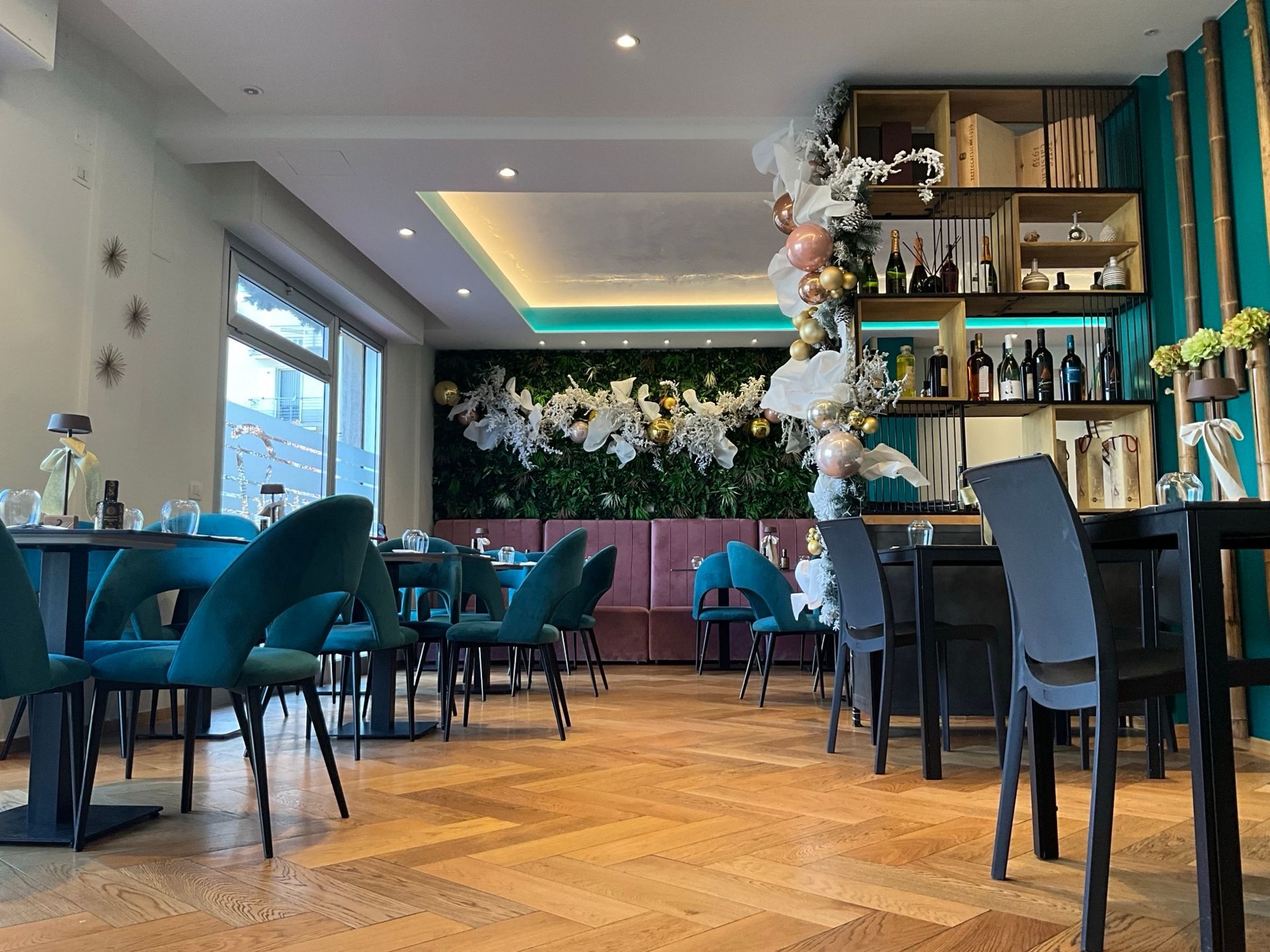 Interno del ristorante con sedie in velluto turchese, pavimenti in legno e una parete con sfondo floreale.