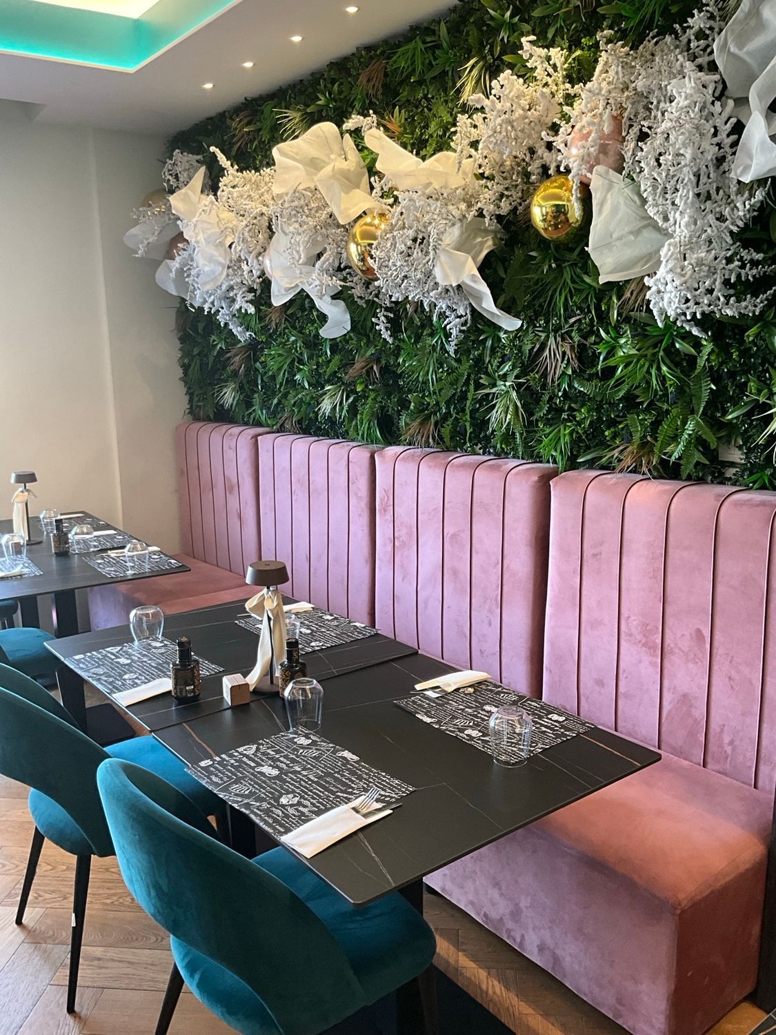 Interno del ristorante con sedie color verde acqua, sedute rosa e una parete decorativa verde.