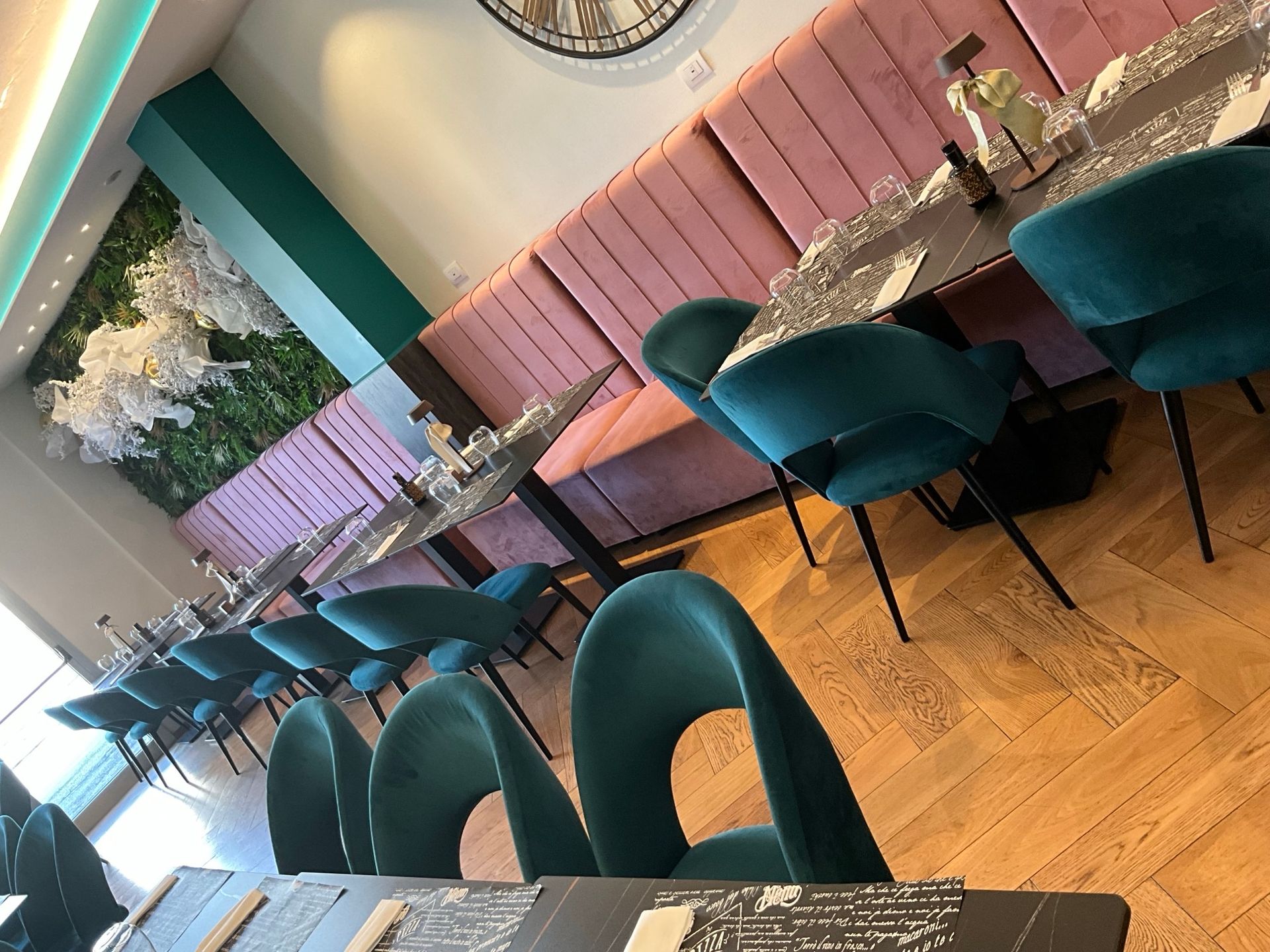 Sala da pranzo del ristorante con sedie color verde acqua, sedute rosa e una parete verde.