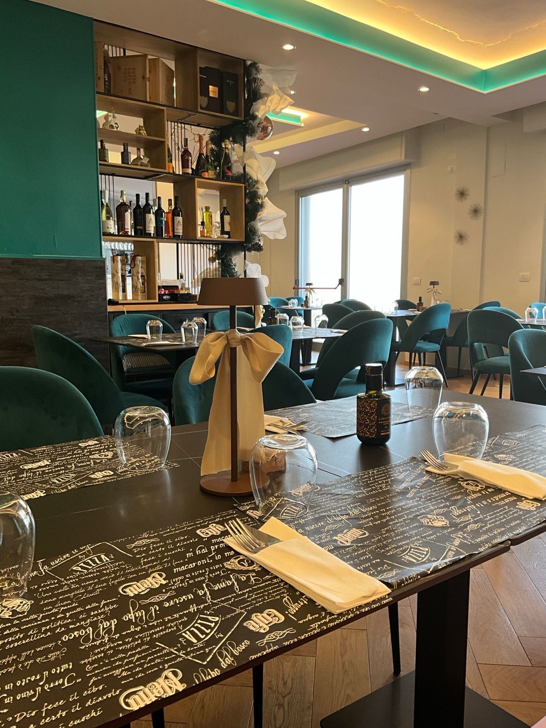 Interno del ristorante con tavoli apparecchiati per la cena; dettagli verdi e marroni.