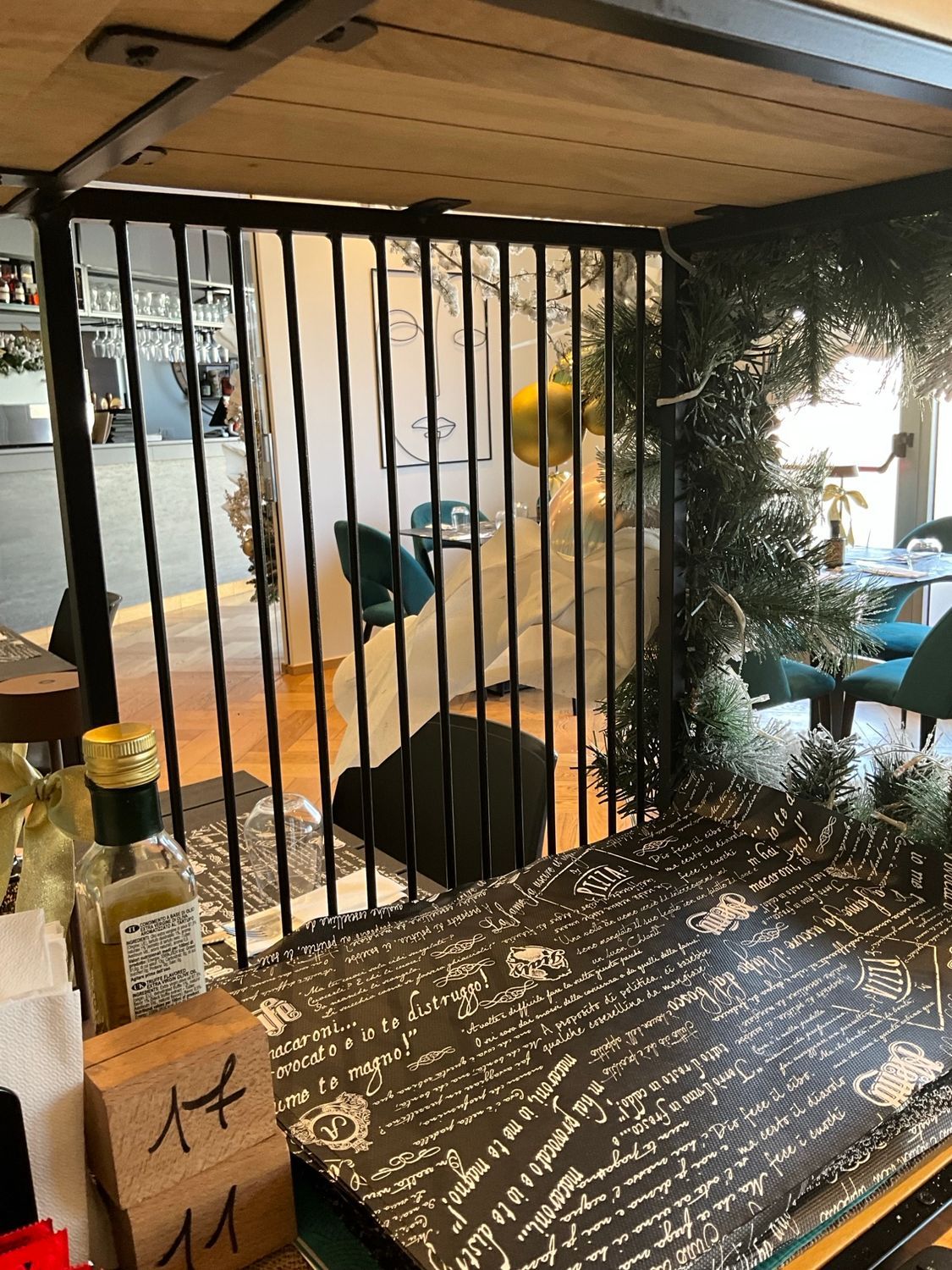 Bar con ferro battuto nero, bancone decorato e scorcio di una zona pranzo con sedie blu e uno specchio.