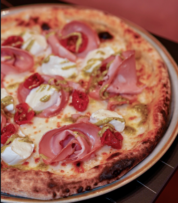 Pizza con prosciutto, mozzarella, pomodori secchi e pesto.