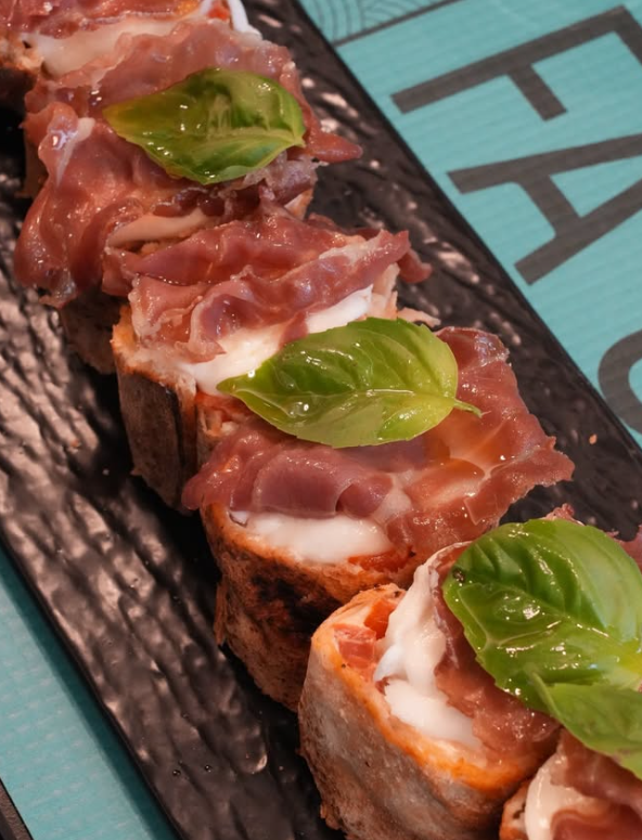 Crostini conditi con prosciutto, mozzarella e basilico su un piatto scuro.