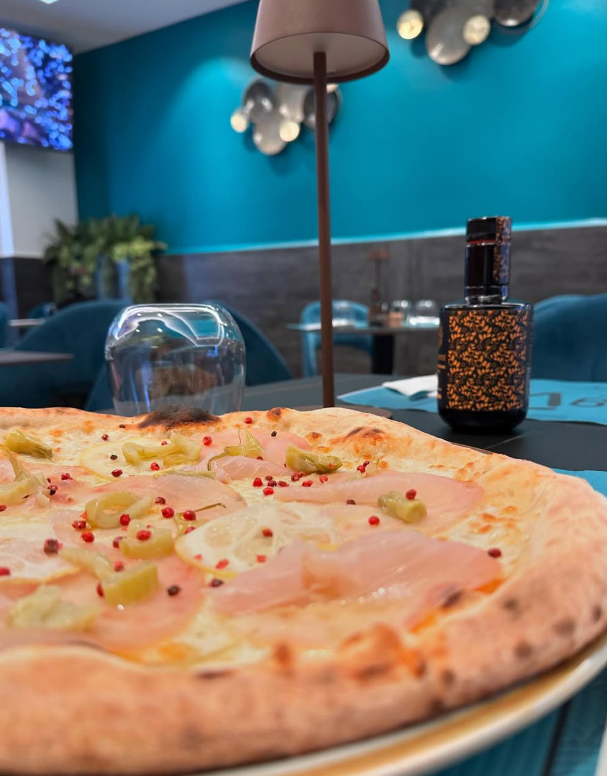 Primo piano di una pizza su un tavolo in un ristorante con pareti color verde acqua.