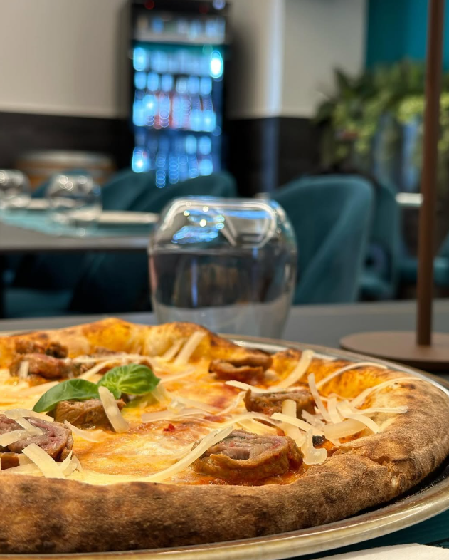 Pizza con salsiccia e formaggio, primo piano, su un piatto di metallo. Sullo sfondo un tavolo di un ristorante.