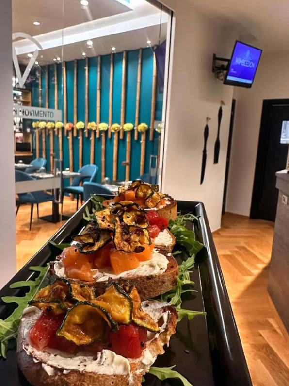 Bruschetta con pomodori e zucchine, su un vassoio nero, in un ambiente da ristorante.