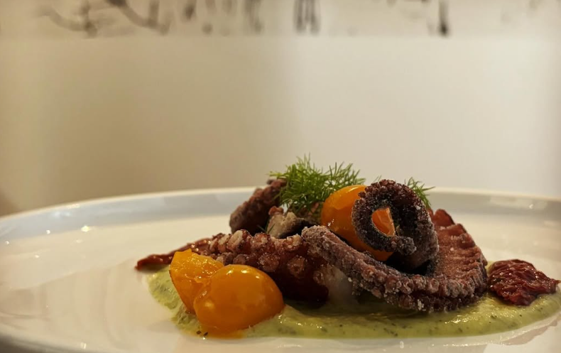 Polpo alla griglia con pomodori gialli, salsa verde e salsa rossa su un piatto bianco.