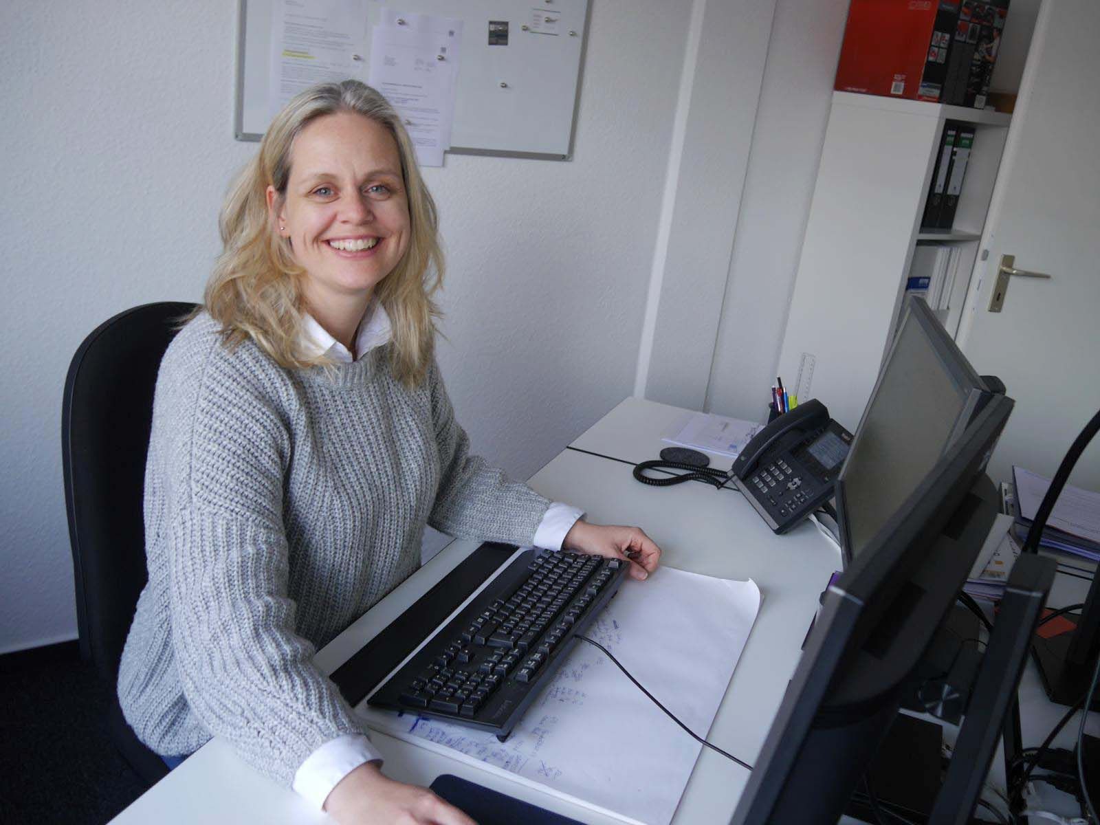 Eine Frau sitzt an einem Schreibtisch mit einem Computer und einem Telefon