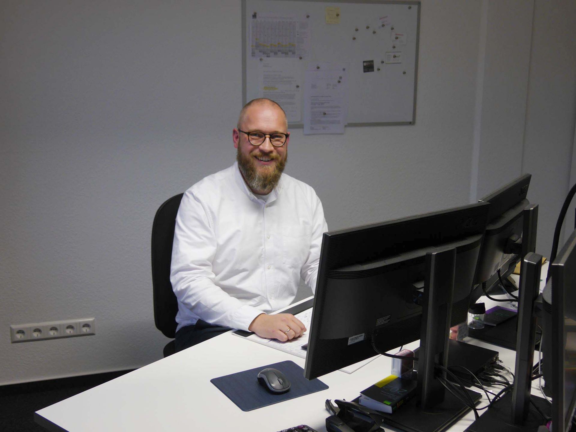 Ein Mann sitzt an einem Schreibtisch vor zwei Computerbildschirmen.