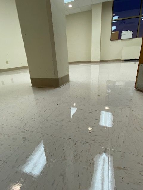 Shiny tiled floor reflecting overhead lights in an empty room, with a beige column and wall.
