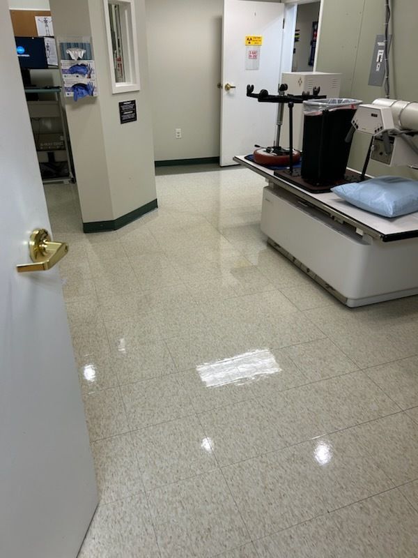 A sterile medical room with a diagnostic imaging table, medical equipment, and a bright, shiny floor.