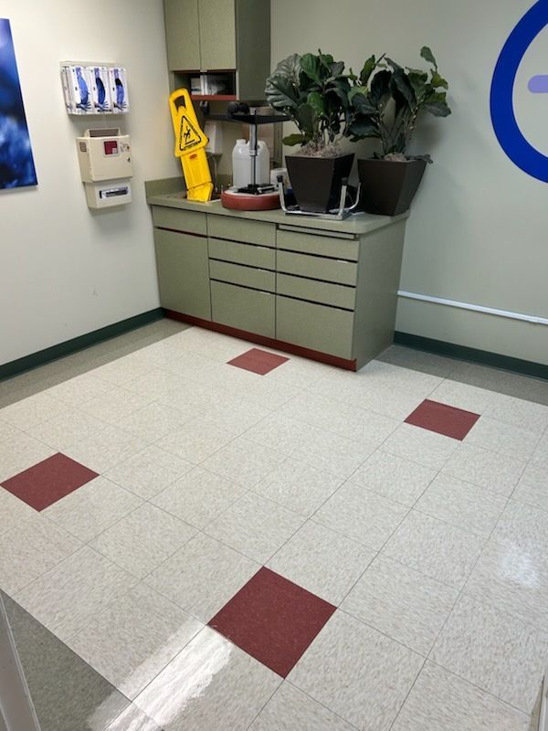 A corner of a room featuring a cabinet, potted plants, a yellow caution sign, and a light floor with red accents.