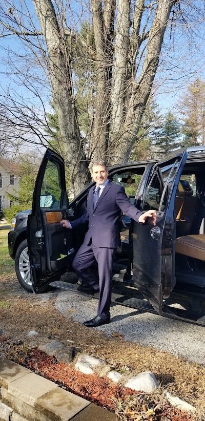 A man in a suit is standing next to a car with the door open.