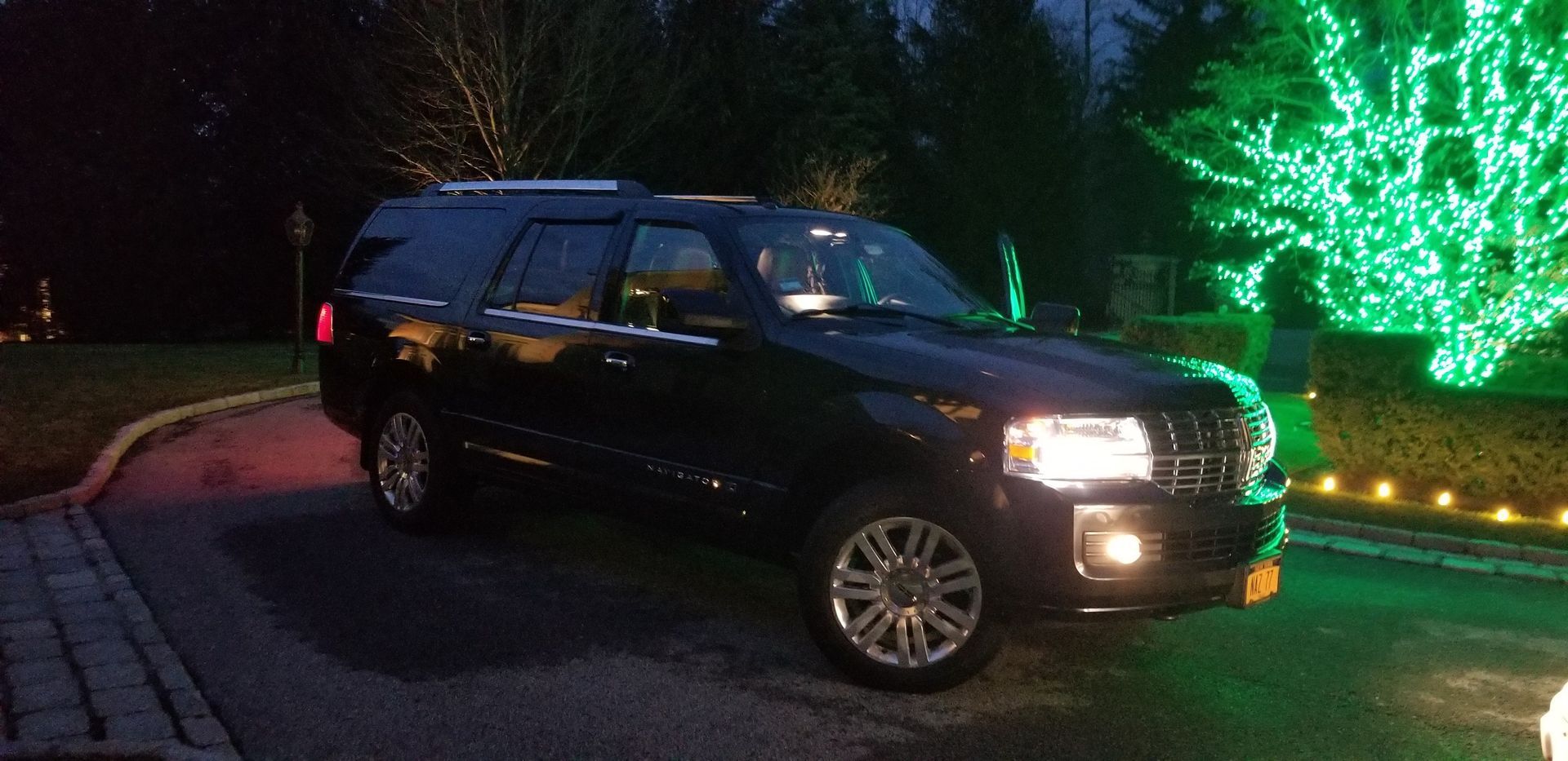 A black suv is parked in front of a christmas tree with green lights.