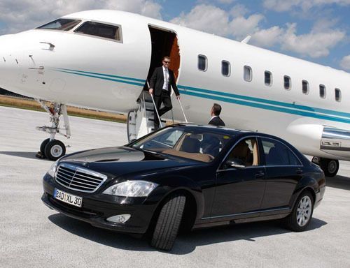 A black car is parked in front of a private jet