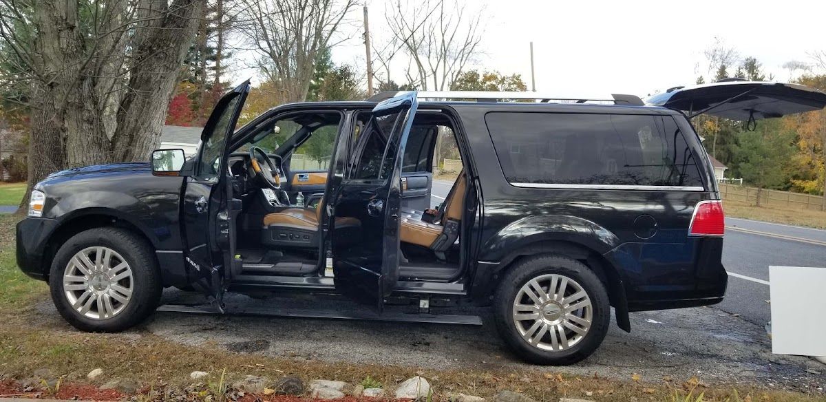 A black ford expedition with its doors open is parked on the side of the road.