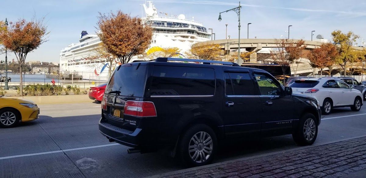 A black suv is parked on the side of the road in front of a cruise ship.
