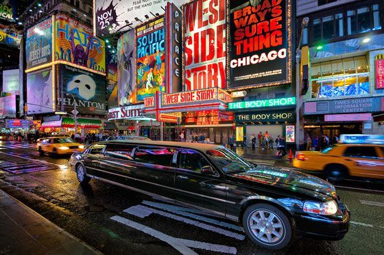 A black limousine is driving down a city street at night.