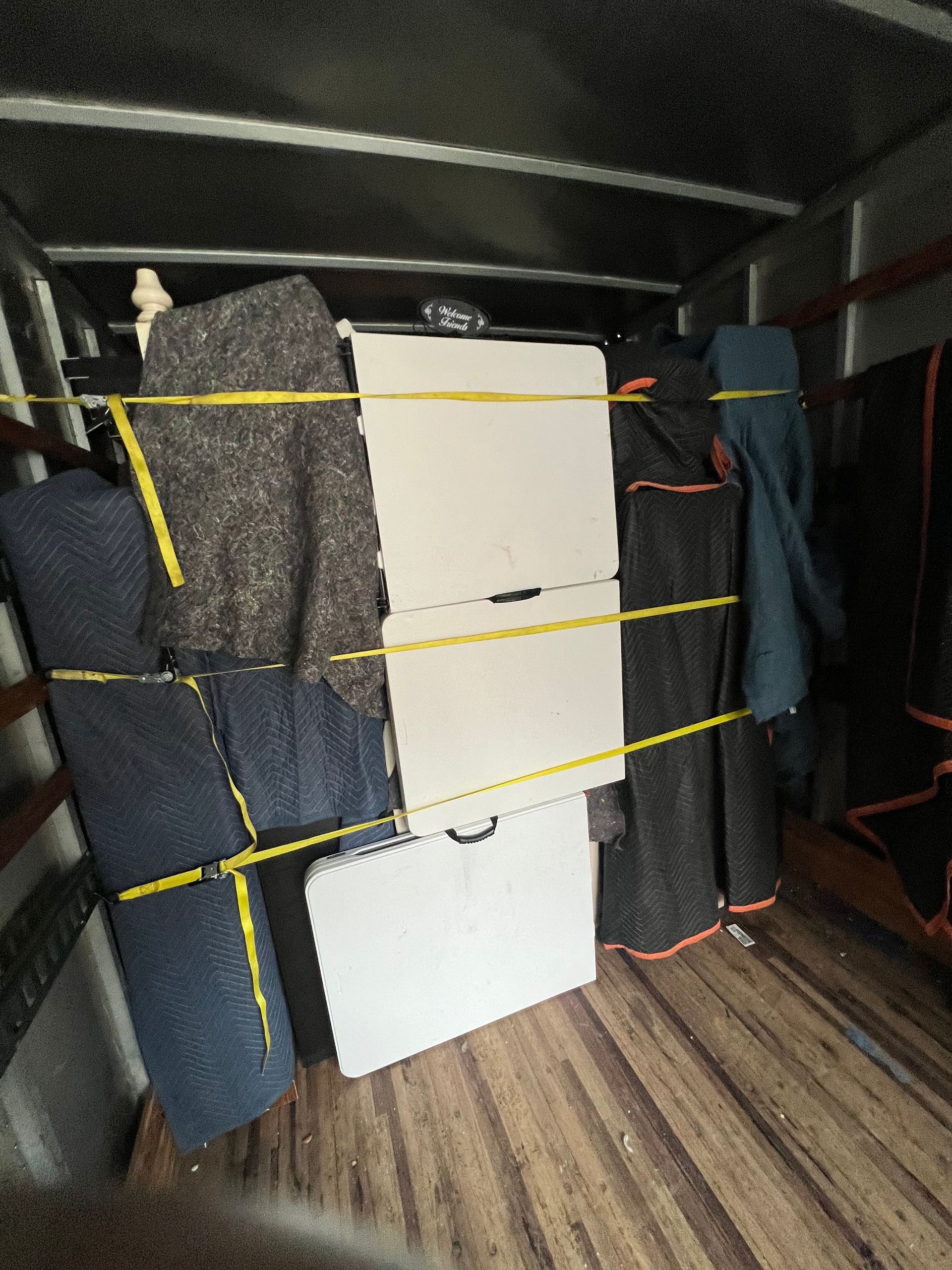 Inside a truck, items are secured with yellow straps. Wrapped furniture and white folding tables are visible.