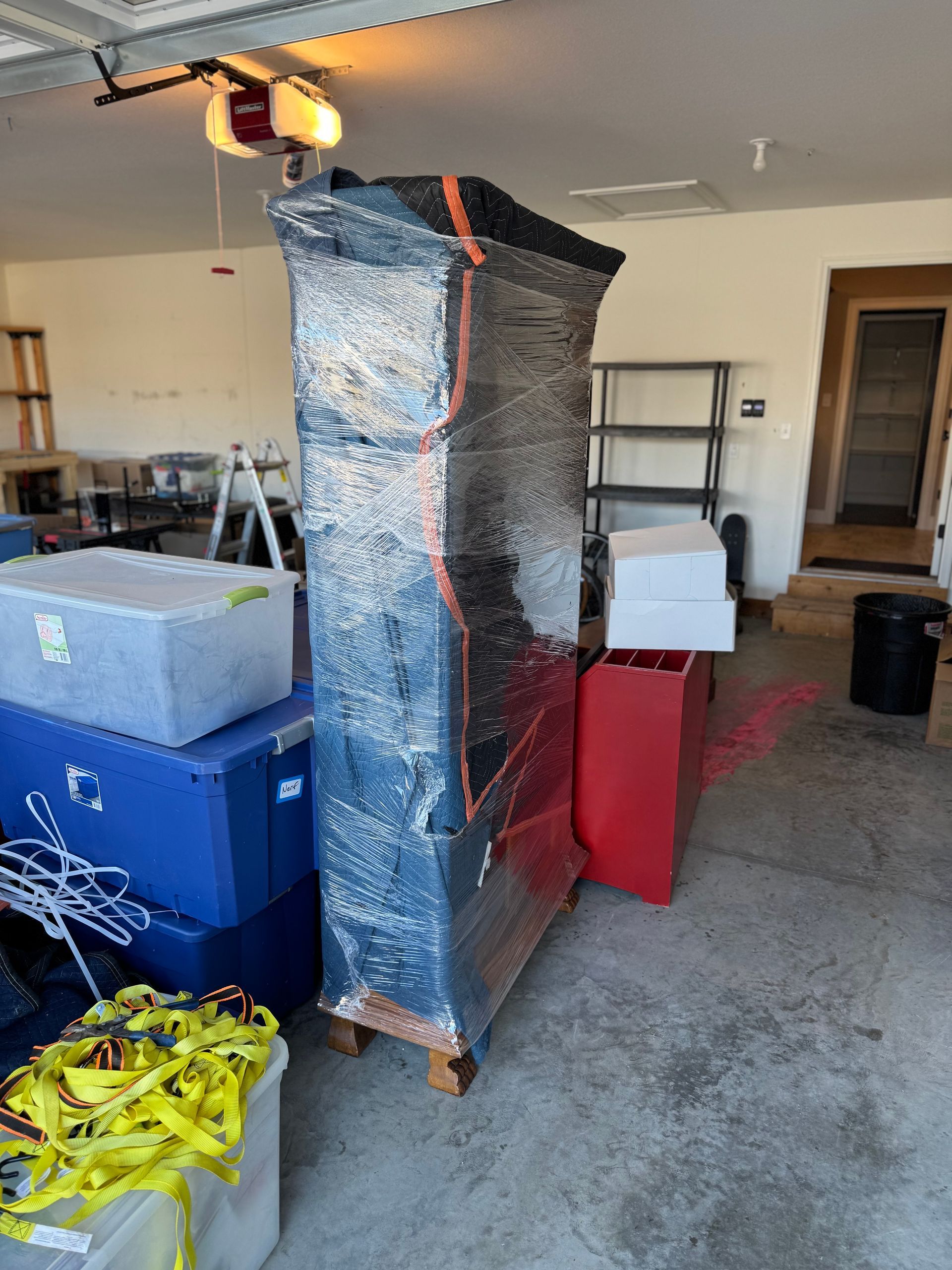 A large, wrapped cabinet in a garage, surrounded by storage bins and boxes.