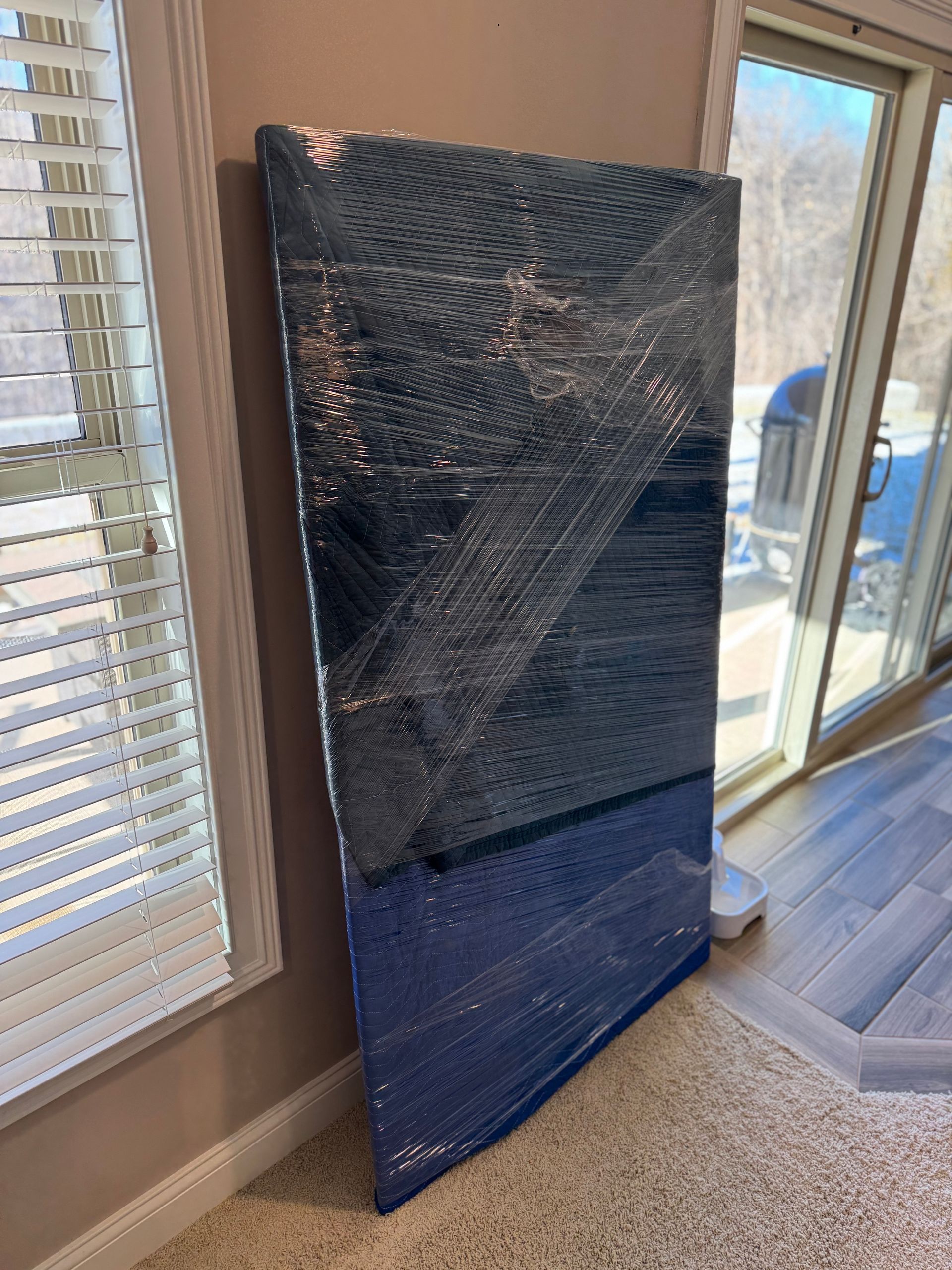 Blue-wrapped rectangular object leaning against a wall next to a window.