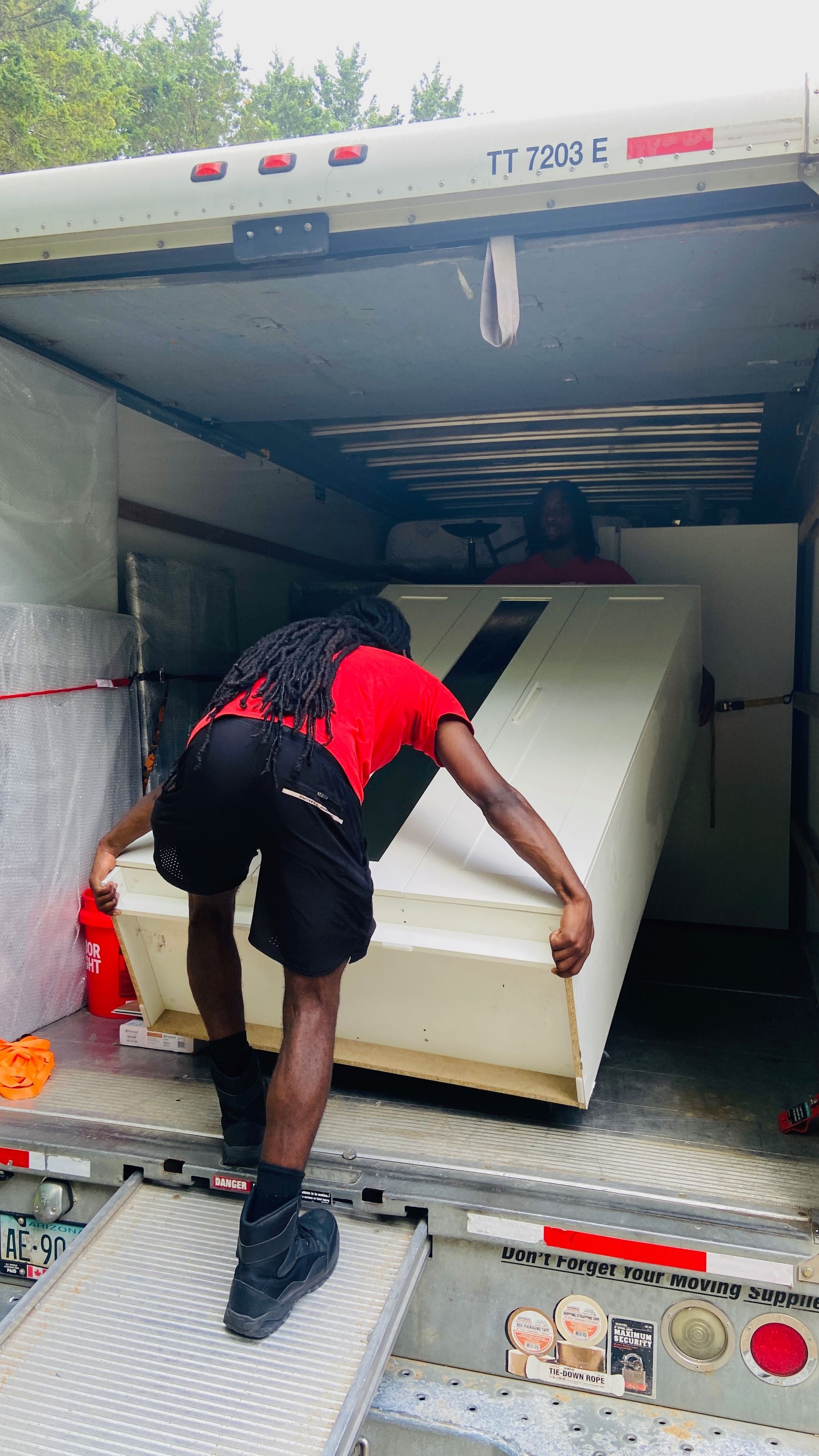 Person in red shirt and black shorts loading large white object into truck.