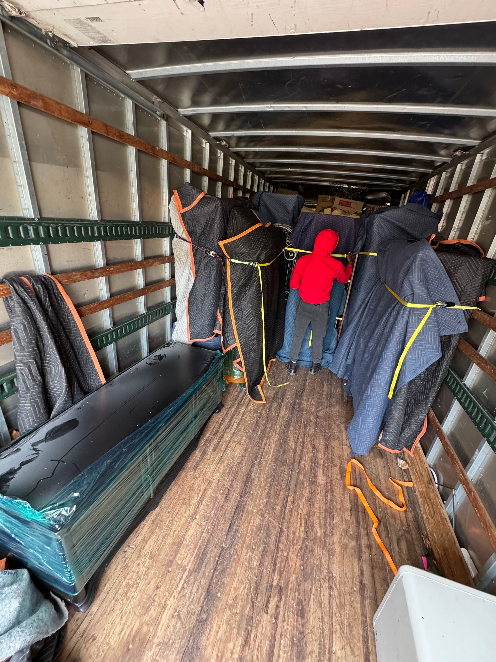 Inside a truck: Person in red jacket amid wrapped items and a long, dark object.