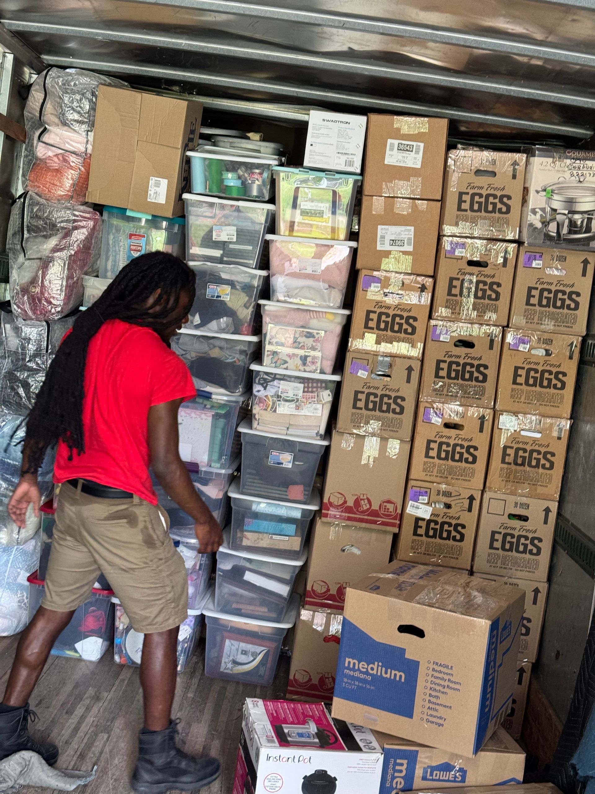 Man in red shirt loads a cluttered truck with boxes and bins; setting is a cargo hold.