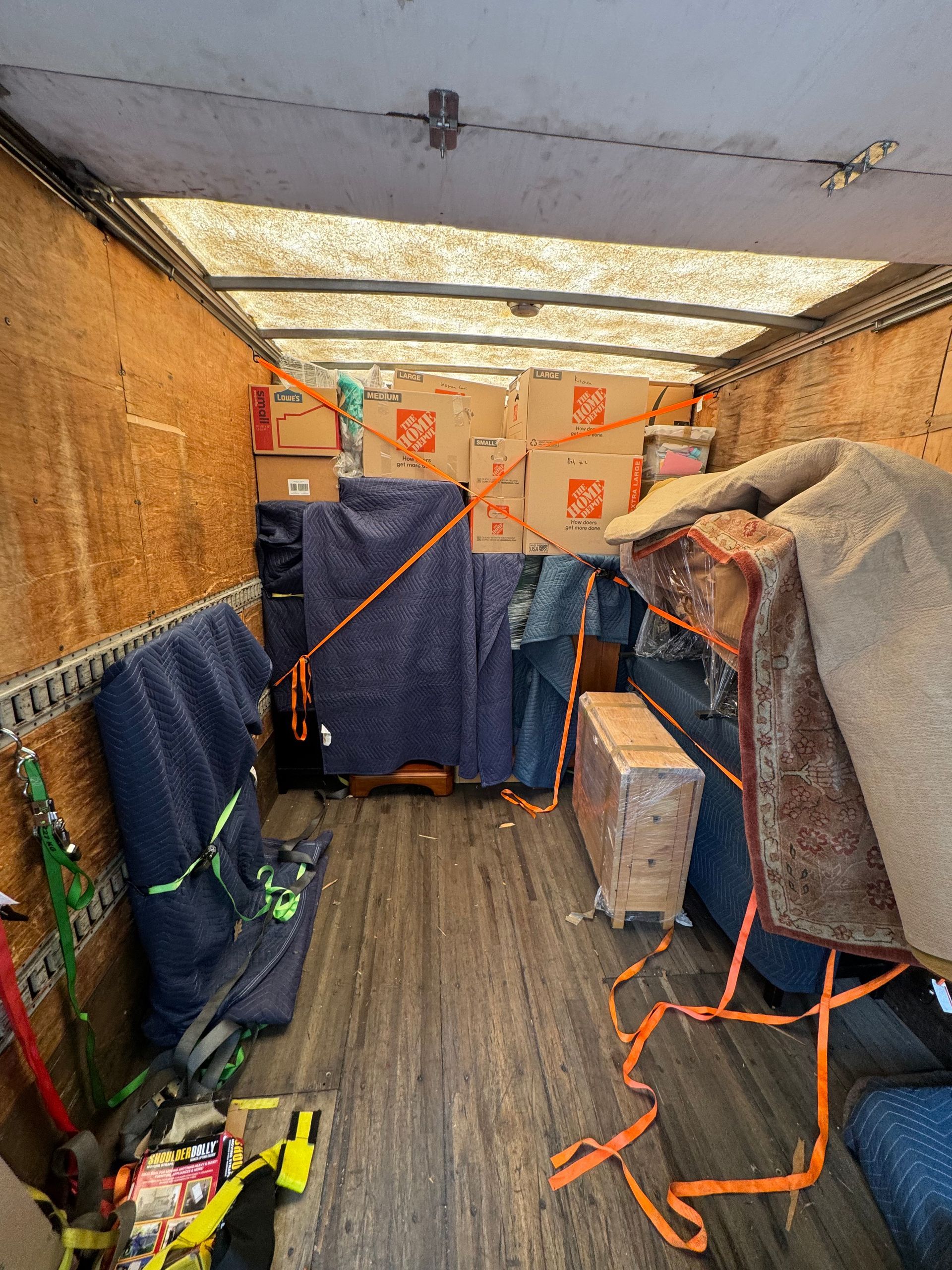 Inside a moving truck, packed with furniture, boxes, and securing straps; preparing for transport.