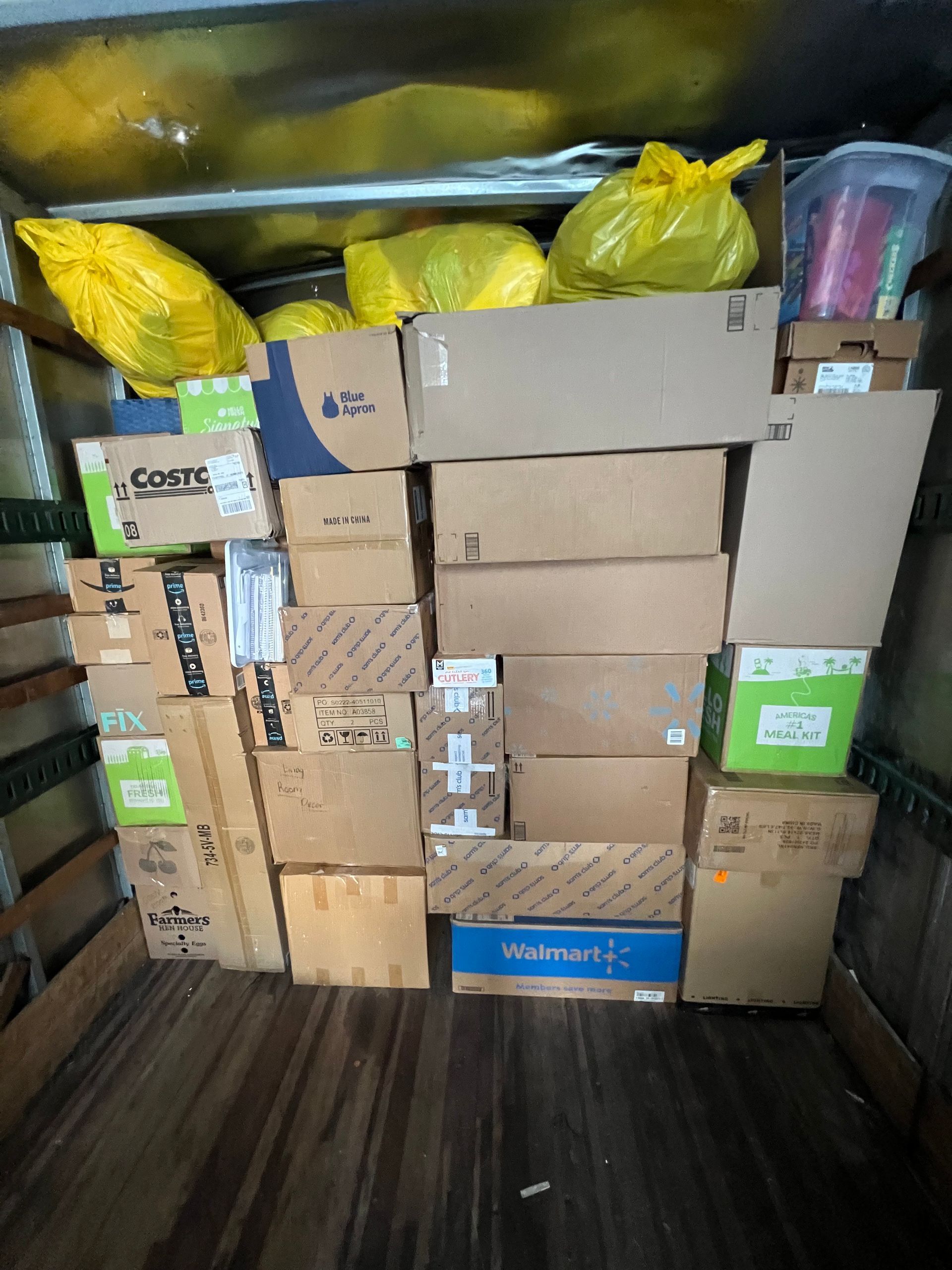 Boxes and bags of packages fill a truck interior. Brown, green, and blue cardboard boxes are stacked.